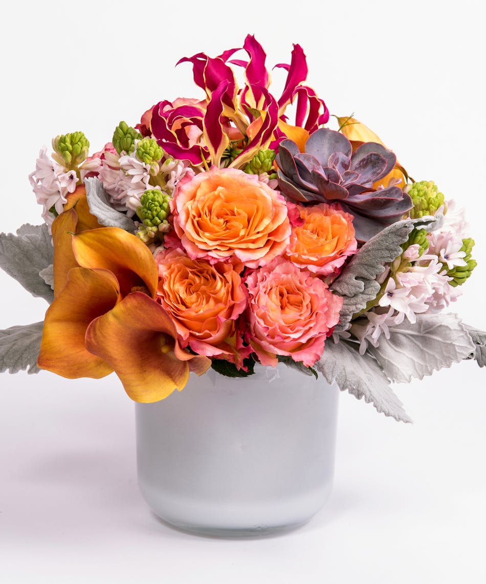 mango calla lilies, orange roses and gloriosa lilies in a white glass cylinder vase