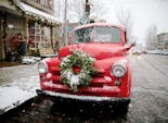 A bright red truck with wreath affixed to its bumper stands in the snow outside our showroom window