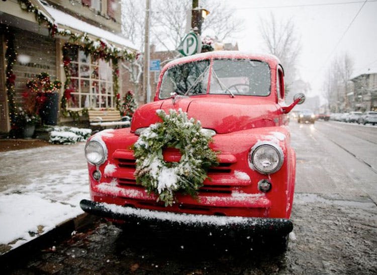 A bright red truck with wreath affixed to its bumper stands in the snow outside our showroom window